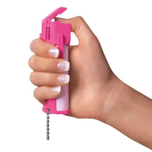 A woman's hand holding a Mace® Personal Model Hot Pink 10% Pepper Spray with a chain.