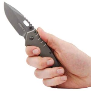 A Titanium Finish Folding Pocket Knife Thumb Open Spring Assisted Gray being held by a person's hand against a white background.