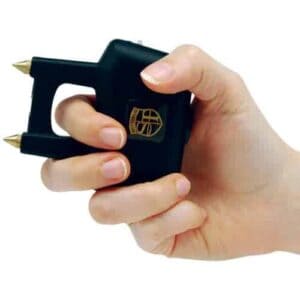 A hand gripping a black Spike Stun Gun with a gold handle, accentuating its sleek and powerful design.