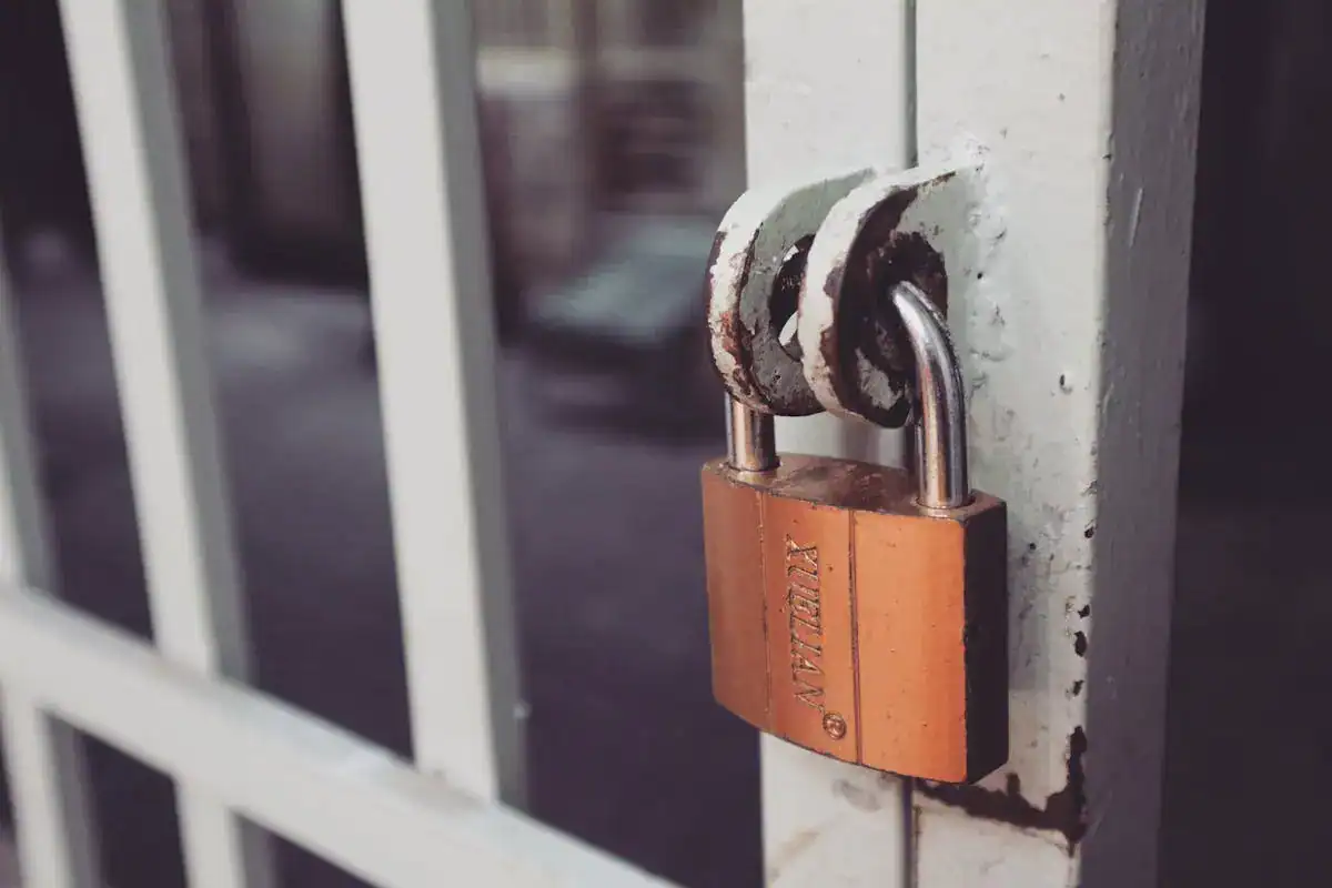 Close-up of a rusted padlock securing a white metal gate.