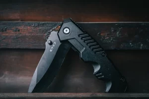 A black folding knife with the blade partially open, resting on a wooden surface.