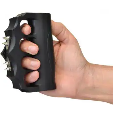 A hand holding a black plastic knuckle duster with metal spikes.