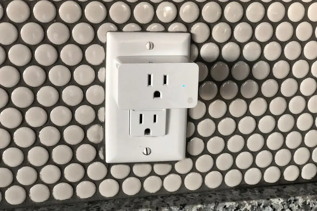 A white electrical outlet with a night light cover, mounted on a wall with round, white tiles.