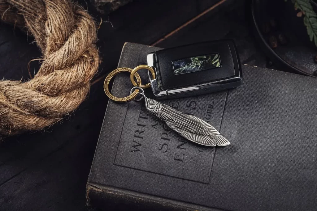 A black car key with a silver leaf keychain rests on a book titled "Writings of Spanish Experiences" beside a coiled rope.