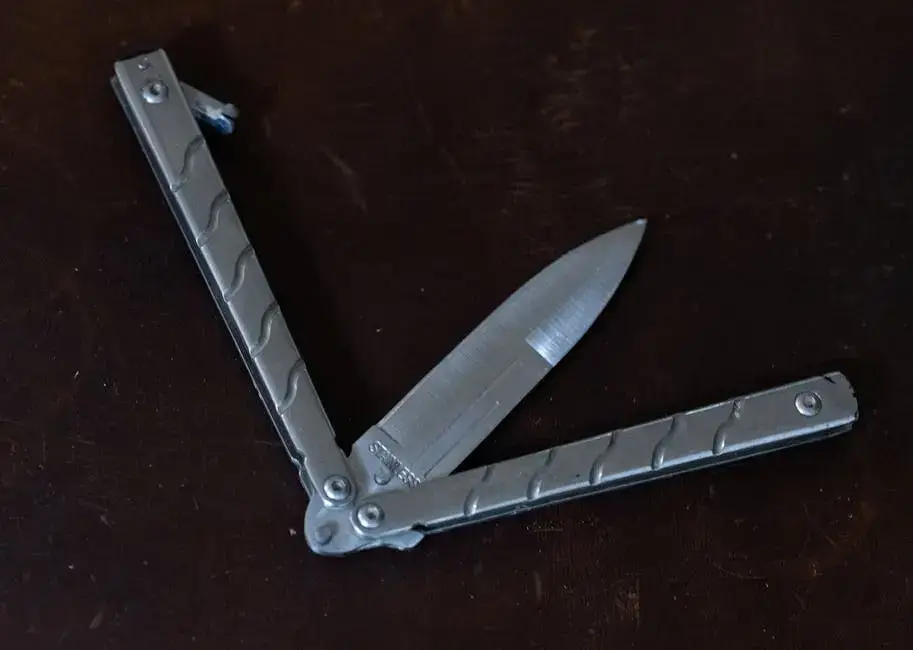 A butterfly knife with a partially open blade on a dark surface.