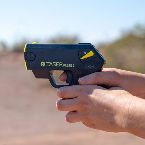 In a natural outdoor setting with clear skies and a softly blurred background, someone grips the Taser Pulse 2.