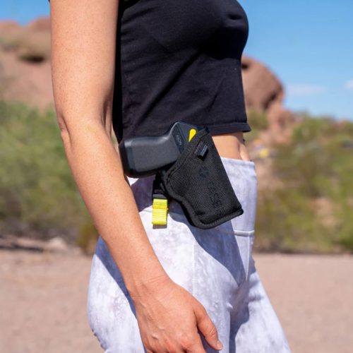 A person wearing a black crop top, gray leggings, and a holster with a Taser Pulse 2 on their right hip stands outdoors.