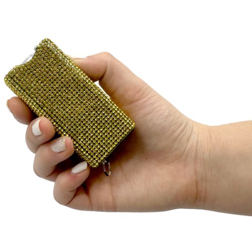 A hand holds a dazzling Rhinestun Keychain Stun Gun—a stunning gold rectangular device adorned with rhinestones and featuring a keyring attachment.