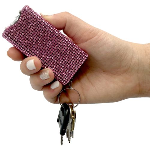 A hand holds the Rhinestun Keychain Stun Gun, a dazzling pink device covered in rhinestones, with attached keys.