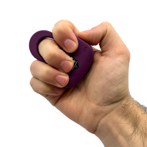 A hand grips a purple oval-shaped ring with a small protrusion, resembling the Sting Ring 18,000,000* Stun Gun, against a clean white background.